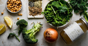 Bone broth for cooking paired with fresh ingredients like leafy greens, broccoli, onion, chickpeas, lemon, and assorted seeds.