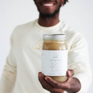 Vegan bone broth in a glass jar held by a hand, featuring a minimalist white label against a yellow background