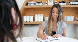 OWL Health Coach smiling while taking notes during a consultation, seated in a natural, wellness-focused setting