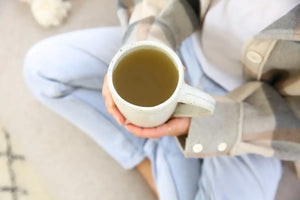 Low sodium bone broth in a ceramic mug, held by a person wearing a plaid jacket and light-wash jeans
