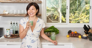 Organic bone broth enjoyed by a smiling woman in a bright kitchen with fresh vegetables and natural light