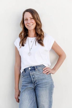 Smiling Lindsey Wilson, OWL founder, wearing a white t-shirt and jeans, standing confidently against a plain white background