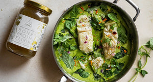 Greens & Coconut Halibut Soup in a skillet with vibrant spinach and herbs, with OWL Organic Bone Broth Elixir jar