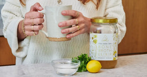 Detox with bone broth using a jar of bone broth elixir, lemon, herbs, and sea salt on a kitchen counter