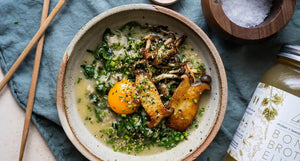 Bowl of ginger greens congee topped with seared mushrooms and an egg yolk, next to a jar of OWL chicken bone broth elixir