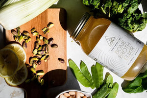 Jar of OWL turkey bone broth with fresh vegetables on a wooden cutting board
